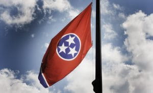 The Tennessee state flag, which features three white stars with five points inside a blue circle with a white outline in the centre of a horizontal red rectangle, and a vertical blue and white rectangle that flies opposite the flagpole. 