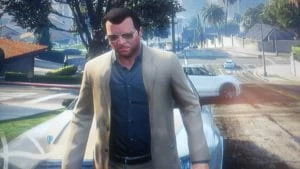 Grand Theft Auto character Michael De Santa in a beige suit with button down shirt and sunglasses standing in front of his default vehicle