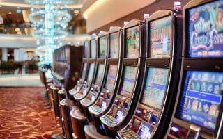 Video slot machines inside a casino with a red carpet containing a busy golden pattern.