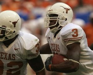 University of Texas player wearing a white uniform and helmet, with orange numbering, lettering, and logo, running with the football