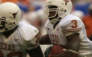 University of Texas player wearing a white uniform and helmet, with orange numbering, lettering, and logo, running with the football