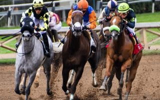 Jockeys riding five horses racing on a dirt track