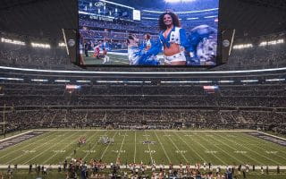 AT&T Stadium which is the home-field of the Dallas Cowboys with their “star” logo at mid-field and “COWBOYS” painted in the end zones. The jumbotron above the field is the largest in the NFL and features on of the Cowboys’ famous cheerleaders.