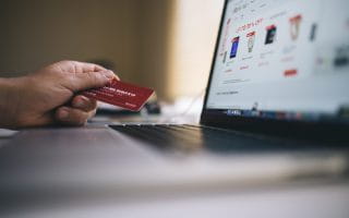 Man's hand holding credit card while online shopping on a laptop computer