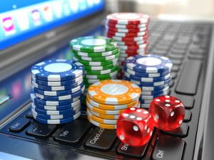 Blue, green, yellow, and red casino chips and a pair of red dice on a laptop keyboard in front of a glowing screen.