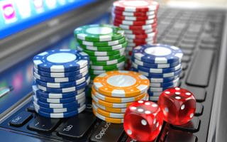 Blue, green, yellow, and red casino chips and a pair of red dice on a laptop keyboard in front of a glowing screen.