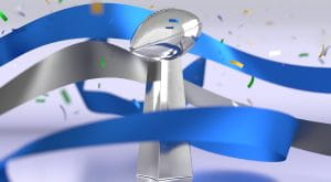 The silver Lombardi Trophy awarded to the Super Bowl Champion team surrounded by multicolored confetti and blue and gray ribbons