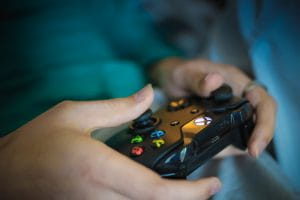 Someone holding a black Xbox One wireless video game controller with its trademark yellow Y, blue X, green A, and red B buttons.