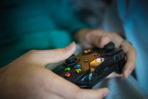 Someone holding a black Xbox One wireless video game controller with its trademark yellow Y, blue X, green A, and red B buttons. 