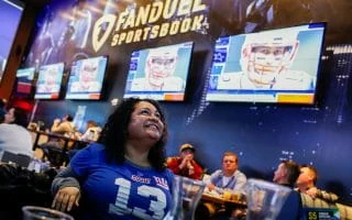 Woman in a New York Giants jersey at a New Jersey sportsbook during the Super Bowl with Tom Brady on the TV screens.