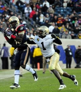 The wide receiver wearing a navy blue jersey makes the catch against a defensive back wearing a white jersey with gold pants. 