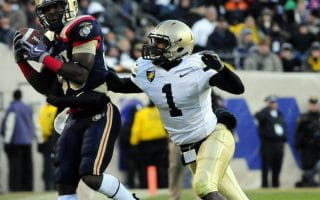 The wide receiver wearing a navy blue jersey makes the catch against a defensive back wearing a white jersey with gold pants.