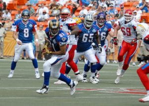 The wide receiver wearing a navy blue jersey makes the catch against a defensive back wearing a white jersey with gold pants