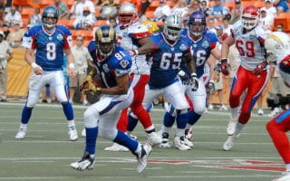 The wide receiver wearing a navy blue jersey makes the catch against a defensive back wearing a white jersey with gold pants