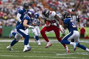 Two defensive players from the NFC wearing blue uniforms converge to tackle the ball carrier of the AFC wearing white in the NFL Pro Bowl.