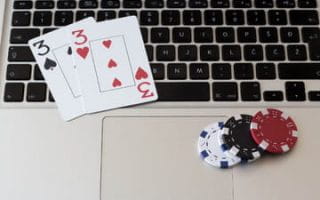 A pair of threes and four poker chips on a MacBook keyboard to represent online poker.