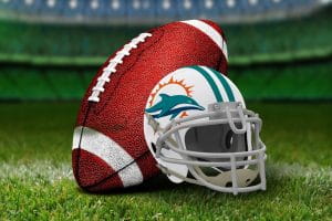 A white Miami Dolphins helmet featuring the teal dolphin, teal stripe, orange splash, and white facemask next to a football