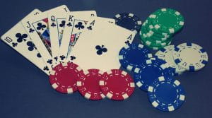 A Royal Flush in clubs on the blue felt of a poker table with poker chips to represent online poker bonuses.