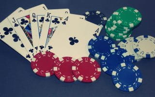 A Royal Flush in clubs on the blue felt of a poker table with poker chips to represent online poker bonuses.