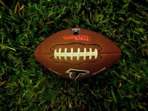 An NFL football with the black and red Atlanta Falcons logo lying on the green turf. 