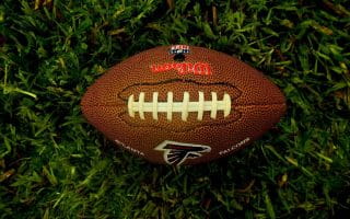 An NFL football with the black and red Atlanta Falcons logo lying on the green turf.