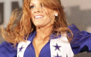 A Dallas Cowboys cheerleader wearing a blue and white blouse tied in the front featuring the Cowboys star logos.
