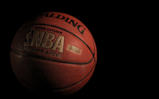 An official NBA orange leather basketball with gold lettering and a black backdrop.