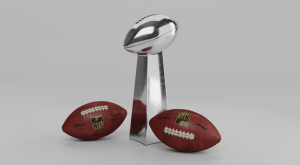 The silver Lombardi Trophy awarded to the Super Bowl Champion with two brown official NFL footballs by its side