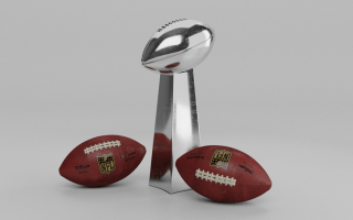 The silver Lombardi Trophy awarded to the Super Bowl Champion with two brown official NFL footballs by its side