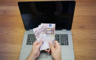 Man holding money above a laptop