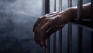 Person’s Hands Behind Bars Over a Dark Background 