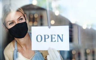 A Shop Assistant Wearing a Mask Holds a Sign Saying Open