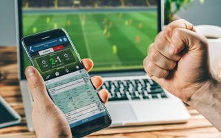 Sports Betting User Victorious Holding Mobile Infront of Laptop