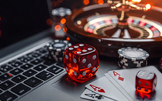 Dice, cards, chips, and a roulette wheel around an open laptop