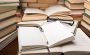 A stack of books with a notepad and a pen