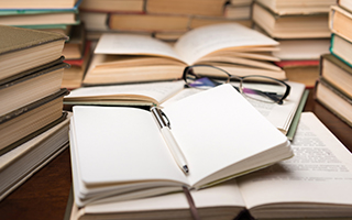 A stack of books with a notepad and a pen